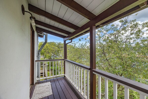 Un balcon en bois avec des balustrades blanches, un plafond blanc et une vue sur les arbres et le ciel.