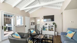 A modern living room with a glass coffee table, a grey sofa, and a blue sofa with floral cushions. - Adorable Rio Del Mar Beach House - Steps to beach! (Aptos)