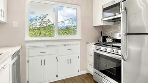 A kitchen with white cabinets, a double window, a stainless steel refrigerator, and a gas stove. - Adorable Rio Del Mar Beach House - Steps to beach! (Aptos)