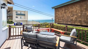 Une terrasse en bois avec des meubles d’extérieur, une vue sur la mer et un bâtiment doté d’un balcon.