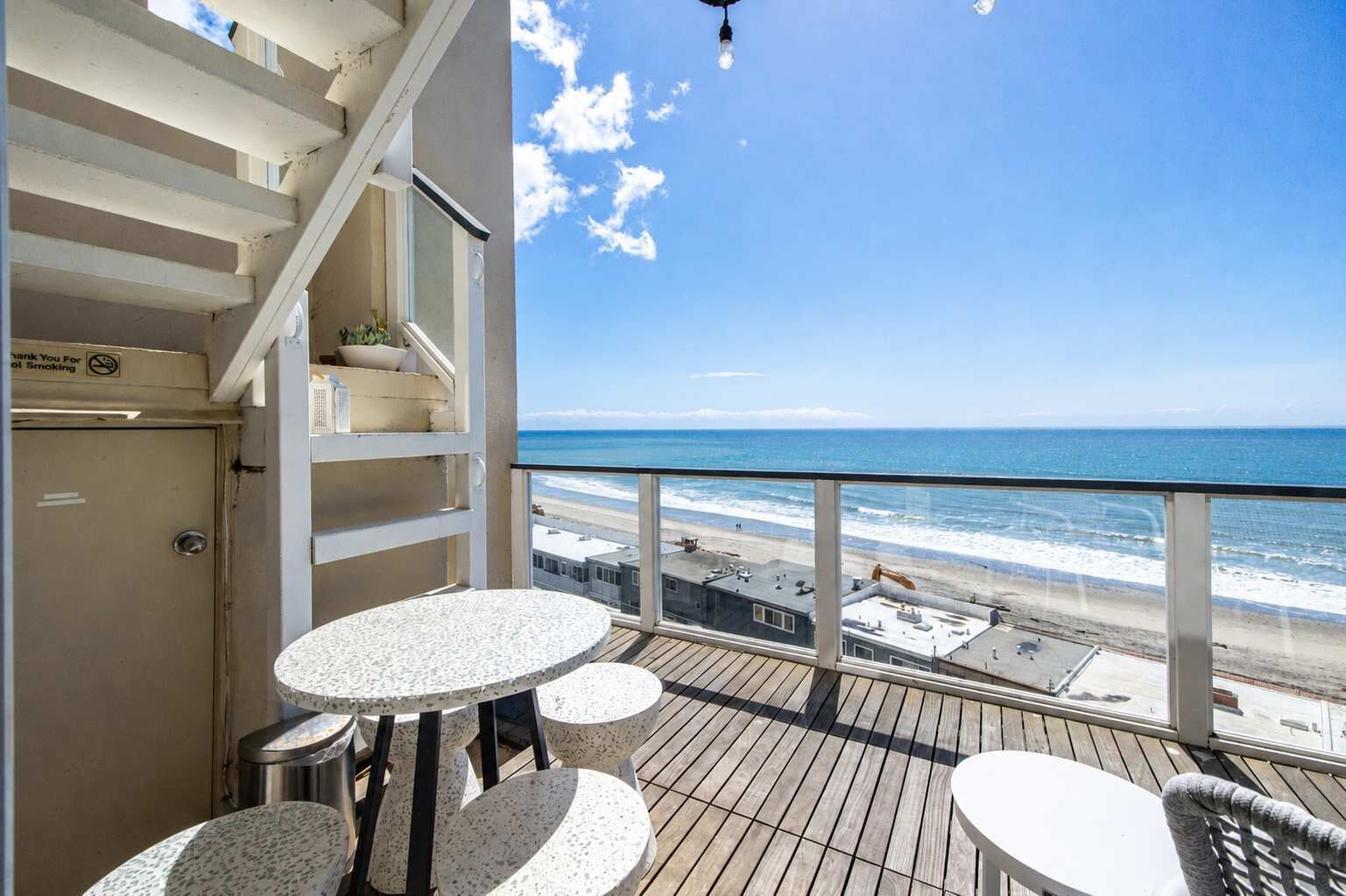Un balcon avec vue sur la plage, un escalier et une table avec des chaises.
