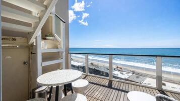 Un balcon avec vue sur la plage, un escalier et une table avec des chaises.