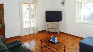 A living room with a television on a cabinet, a chandelier, a sofa, and a coffee table. - Air-conditioned holiday villa 3 bedrooms sea view (CAVALAIRE SUR MER)