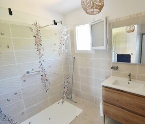Ein Badezimmer mit Dusche, Waschbecken, Spiegel und Fenster.