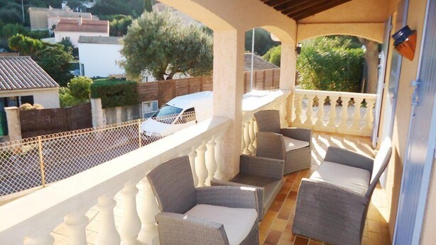 A balcony with wicker furniture, a white railing, and a view of a residential area. - Air-conditioned holiday villa 3 bedrooms sea view (CAVALAIRE SUR MER)