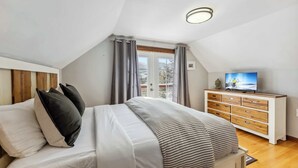 Ein Schlafzimmer mit einem Bett, einem Schminktisch, einem Fernseher und einem Fenster mit Vorhängen.