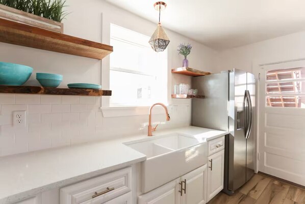 A modern kitchen with white cabinetry, a stainless steel refrigerator, and a copper faucet.