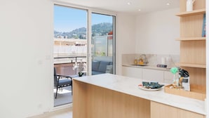 A modern kitchen with a marble countertop, wooden shelving, and a sliding glass door leading to a balcony.