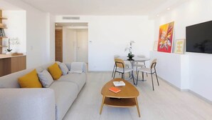 A modern living room with a sofa, coffee table, dining table, chairs, and artwork on the walls.