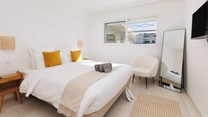 A modern bedroom with a bed, bedside tables, a chair, a large mirror, and a window.