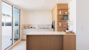 A modern kitchen with a central island, wooden cabinetry, and a view through a glass door.