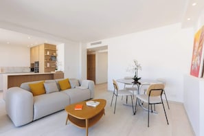 Ein modernes Wohnzimmer mit Sofa, Couchtisch, Esstisch, Stühlen und einer Küche im Hintergrund.