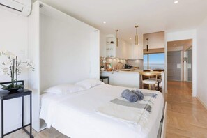 Une chambre d’hôtel moderne, équipée d’un lit, d’une table de chevet et offrant une vue sur la cuisine et l’espace repas.