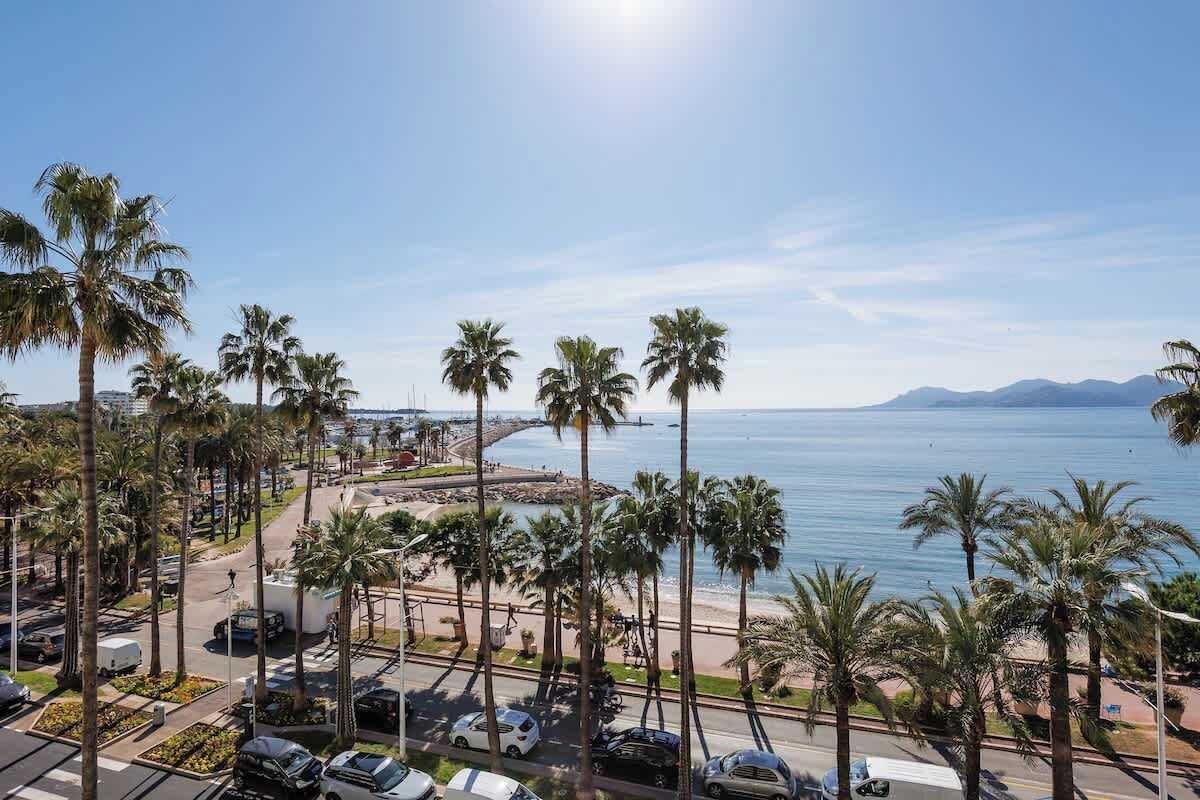 Eine Küstenstraße mit Palmen, einem Strand und freiem Blick auf das Meer.