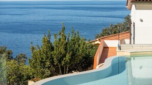 A pool with a view of the sea, surrounded by trees and a building with a tiled roof. - Villa with swimming pool and sunset view (Marciana Marina)