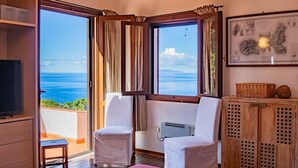 A room with a large window overlooking the sea, a white chair, a small table, and a wall-mounted air conditioner. - Villa with swimming pool and sunset view (Marciana Marina)