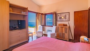 A bedroom with a bed, a TV, a wardrobe, a chair, a desk, and a window with a view of the sea. - Villa with swimming pool and sunset view (Marciana Marina)