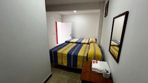 Ett litet hotellrum med två sängar, ett träbord vid sängen, en spegel och en dörr som leder till ett annat rum.
