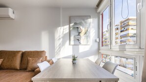 Una sala de estar moderna con un sofá, una mesa de comedor de madera y vista a un edificio a través de una ventana.