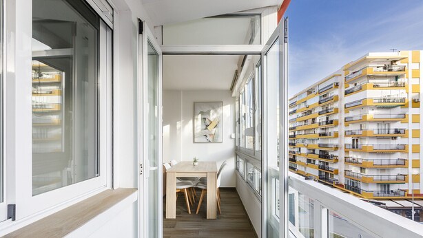 Un balcón estrecho con una mesa y sillas de comedor, una planta pequeña y un cuadro en la pared.