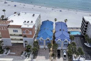 A beachfront hotel with multiple-story buildings, a swimming pool, and a beach in the background.
