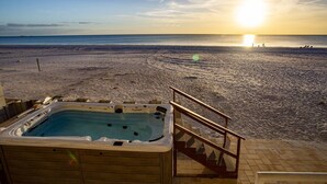 A hot tub on a wooden deck overlooking a beach with a sunset in the background.