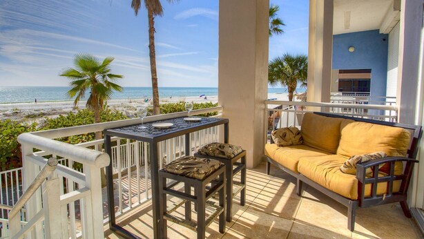 A balcony with a view of the beach, a table with chairs, and a sofa.