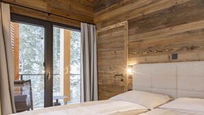 En stuga med träpanel, inredd med en säng, en stol och ett bord intill ett stort fönster.