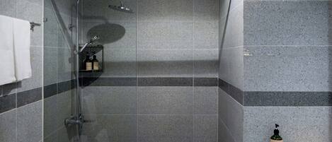 A modern shower with a glass enclosure, a handheld showerhead, and a bottle of hand wash soap on the counter.