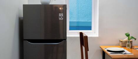Una cocina compacta con refrigerador incorporado, ventana con vistas, mesa de comedor de madera y una silla.