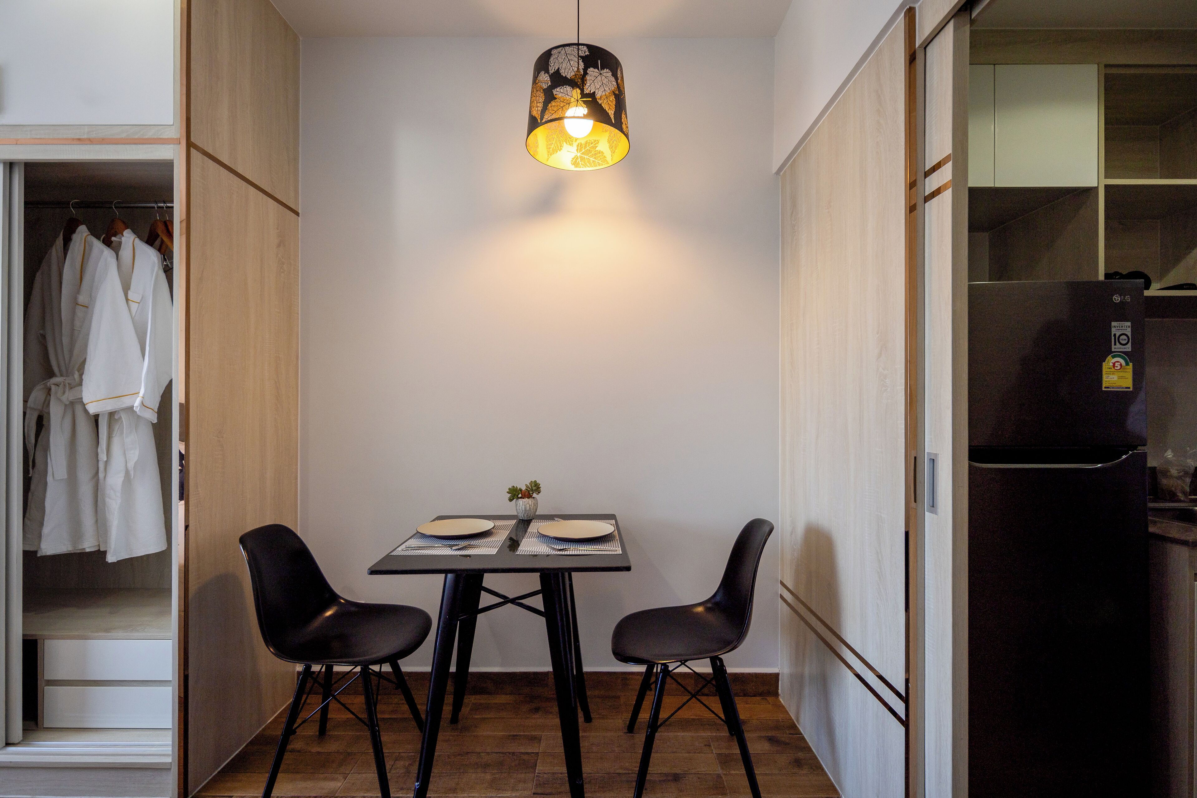 A compact kitchen with a dining table, two chairs, a hanging light fixture, and a refrigerator.