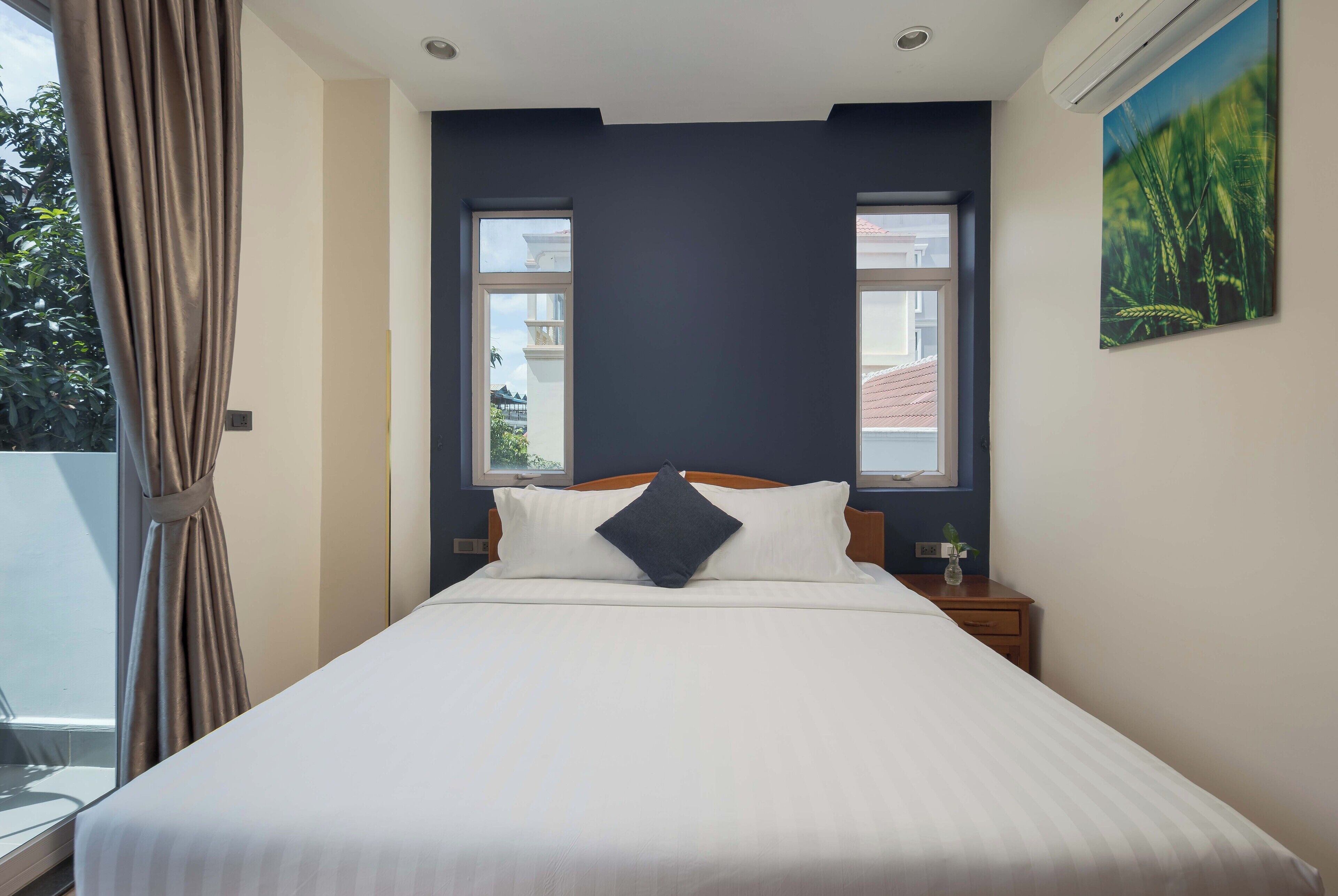 A neatly made bed with a dark pillow, a wooden headboard, and two bedside tables with lamps.