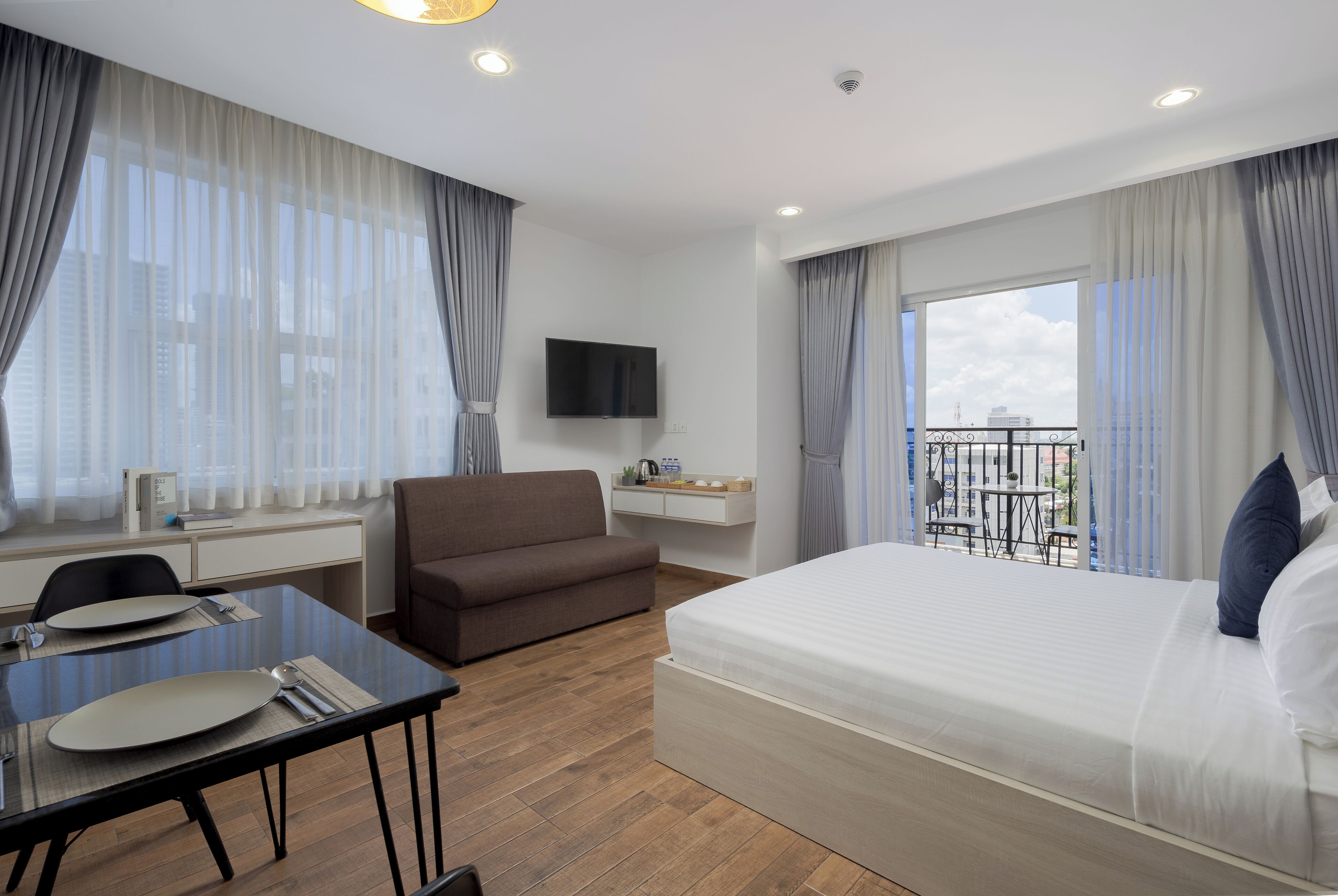 A hotel room with a bed, a desk, a chair, a TV, and a balcony with a view of the city.