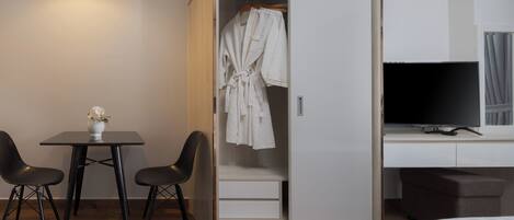 A modern hotel room with a walk-in closet, a desk with a flat-screen TV, and a dining area with two chairs and a table.