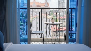 A hotel room with a balcony, a bed, a chair, a small table, and a potted plant.