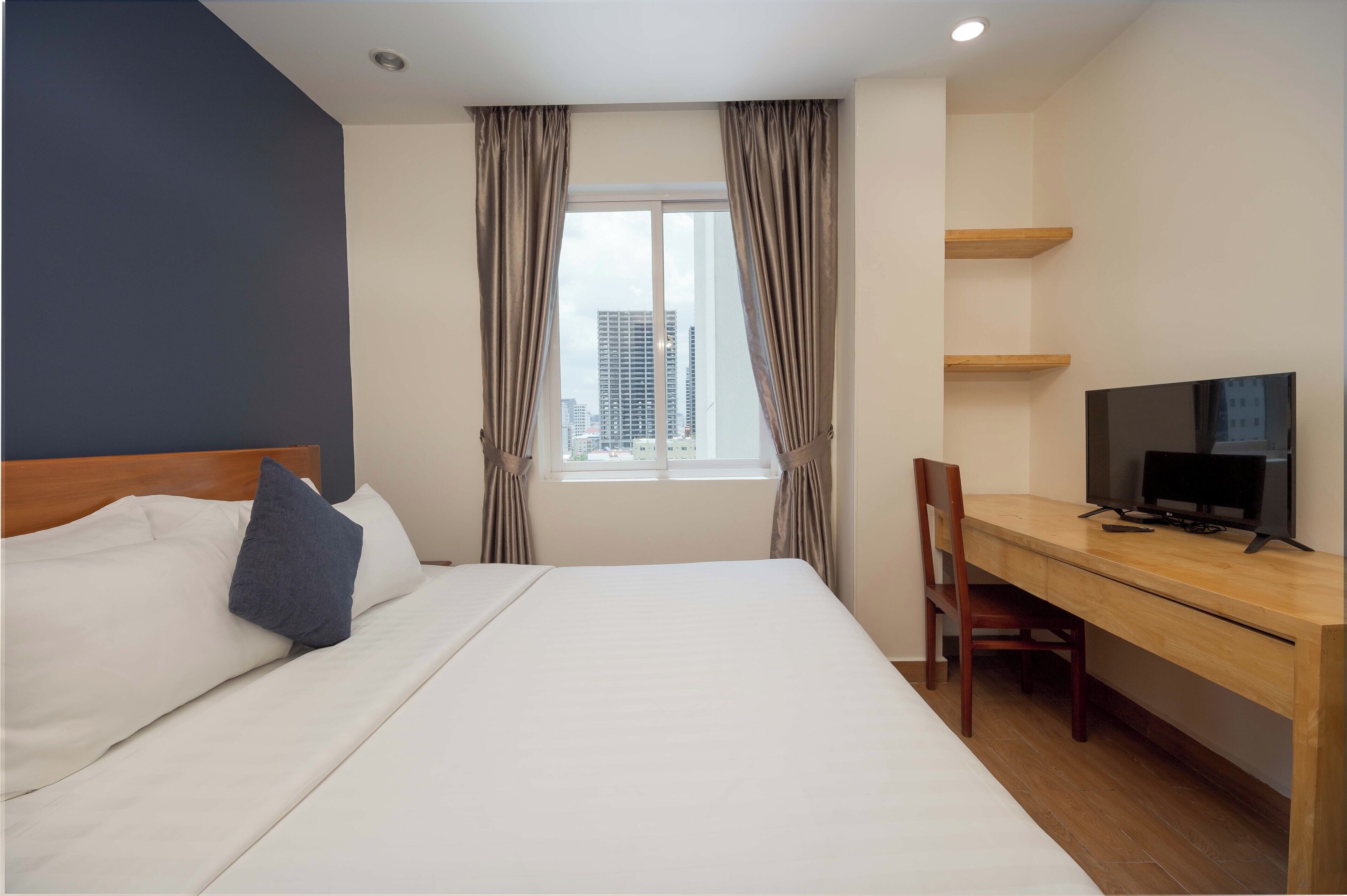 A hotel room with a bed, a desk with a TV, and a window with curtains.
