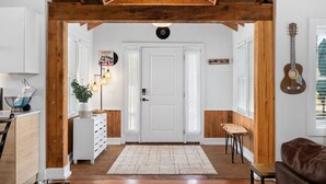 Une pièce avec un plafond en bois, une porte blanche, une guitare accrochée au mur et une plante près de la porte.