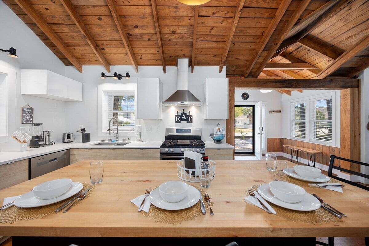A modern kitchen with wooden beams, white cabinetry, and a central island with dining set.