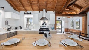 Une cuisine moderne avec des poutres en bois, des meubles blancs et un îlot central agrémenté d’un ensemble de table et de chaises.