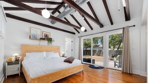 Une chambre à coucher avec un lit en bois, une table de chevet, une lampe, une fenêtre avec des rideaux et une vue sur l’extérieur.