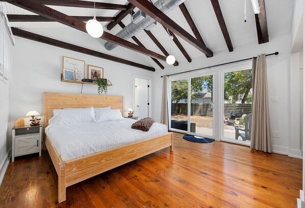 Une chambre à coucher avec un lit en bois, une table de chevet, une lampe, une fenêtre avec des rideaux et une vue sur l’extérieur.