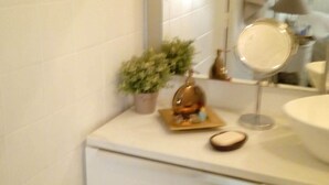 A bathroom with a white vanity, a mirror, a small potted plant, and a toilet.