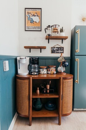A kitchen with a coffee maker, a coffee mug, a sign saying 'Coffee and Cocktails,' and a vintage poster on the wall.