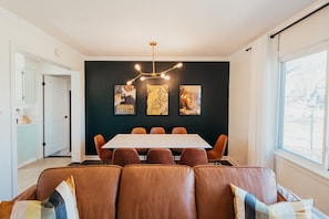 Un'area pranzo con tavolo e sedie, una parete scura con opere d'arte, un lampadario e una finestra.