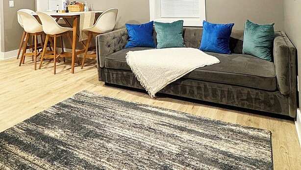 A living room with a grey sofa, blue and green cushions, a wooden dining table with chairs, and a patterned rug. - 1BR Oasis Escape in SE Atlanta (Atlanta)