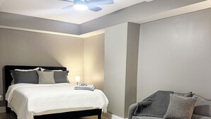 A bedroom with a bed, a gray sofa, a ceiling fan, and a patterned rug. - 1BR Oasis Escape in SE Atlanta (Atlanta)