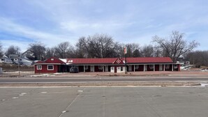 A red motel with a single-story structure, a covered parking area, and a clear sky. - Big Red motel (Laurel)