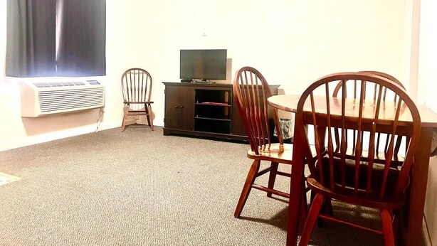 A room with a carpeted floor, a television on a stand, and two wooden chairs. - Big Red motel (Laurel)