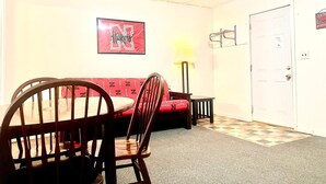 A dining area with a red upholstered booth, a wooden dining table, and chairs. There is a framed picture on the wall and a lamp on the floor. - Big Red motel (Laurel)