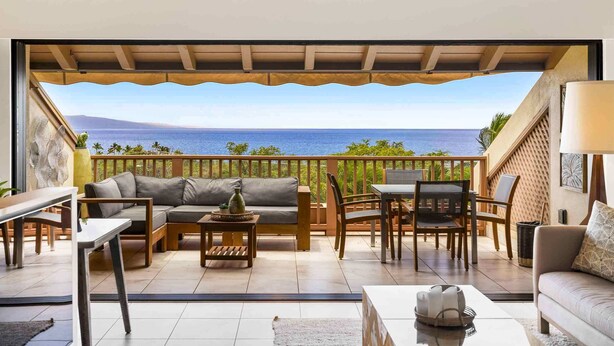 Een balkon met uitzicht op zee, voorzien van een bank, stoelen en een tafel.